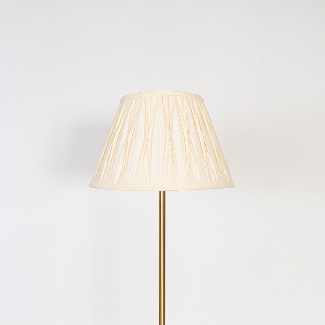 Closeup of pleated white lampshade with golden lamp base showing fine fabric texture and warm light glow.