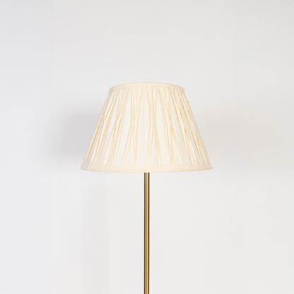 Closeup of pleated white lampshade with golden lamp base showing fine fabric texture and warm light glow.