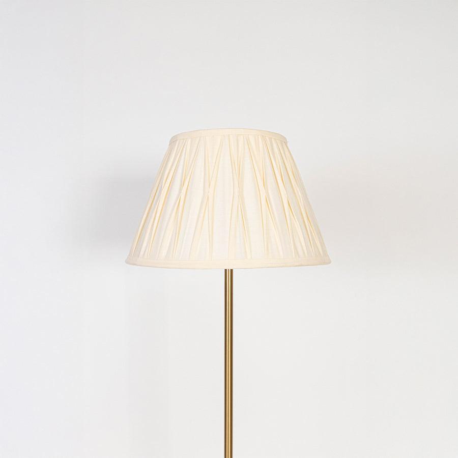 Closeup of pleated white lampshade with golden lamp base showing fine fabric texture and warm light glow.
