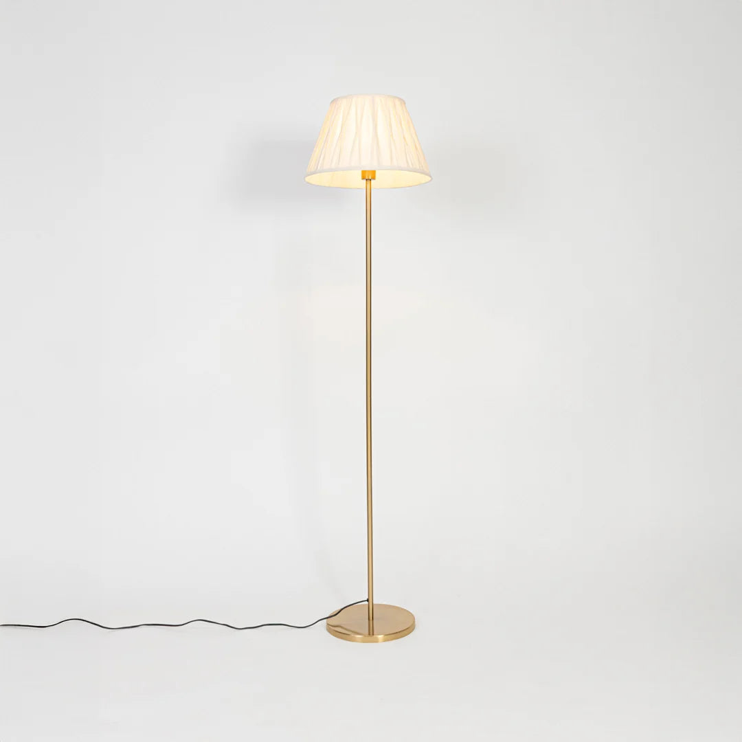 Brass floor lamp with pleated fabric shade casting warm ambient light for elegant living room and bedroom decor.