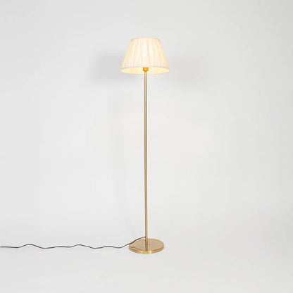 Brass floor lamp with pleated fabric shade casting warm ambient light for elegant living room and bedroom decor.