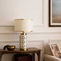 Modern white and gold ceramic table lamp styled on a wooden console against elegant wall paneling creating a sophisticated decor look.