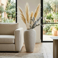 White textured floor vase with pampas grass placed beside sofa for elegant modern decor styling.