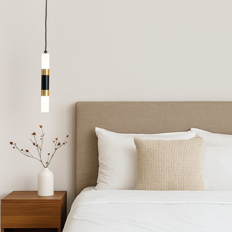 Stylish black and gold cylindrical pendant light glowing above bedside table with ceramic vase in cozy bedroom interior.