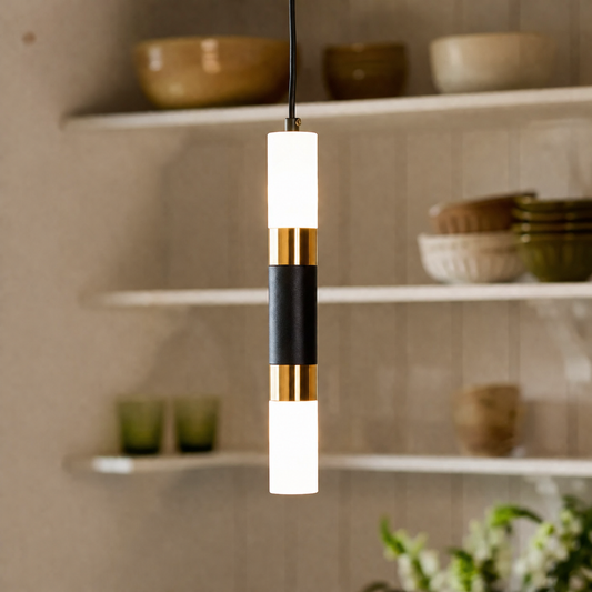 A modern cylindrical pendant light hanging in a kitchen setting, featuring white frosted glass shades, a black leather wrap, and gold metal accents.