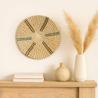 Woven round wall basket styled above wooden console with ceramic vases and dried grass creating warm natural living room Decor.