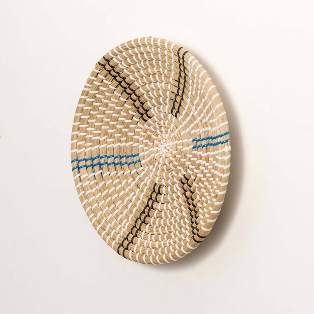 Side view of handcrafted natural cream seagrass wall basket with blue and grey striped spokes for boho wall decor display.