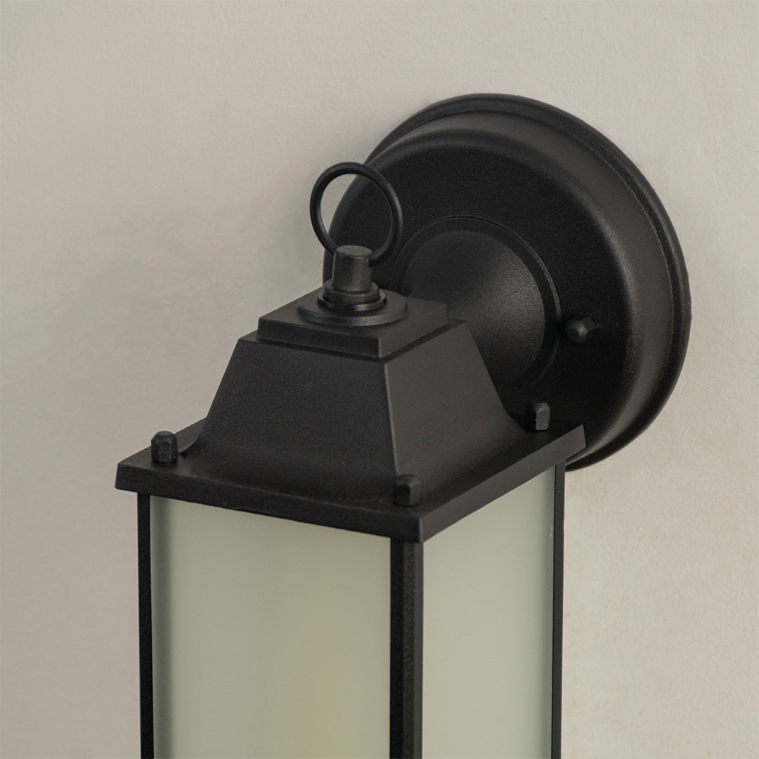 Minimalist black outdoor wall lantern closeup image showing top ring loop detail matte finish and frosted glass panel.