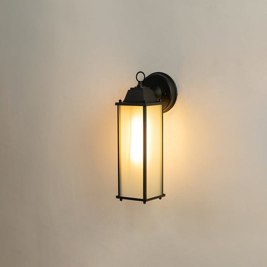 Black outdoor wall lantern displayed on a white background featuring a tall frosted glass shade and linear metal borders.
