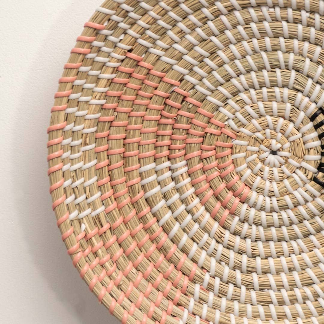 Detailed closeup of handcrafted natural seagrass wall basket with pink woven stitched geometric accents for boho decor.