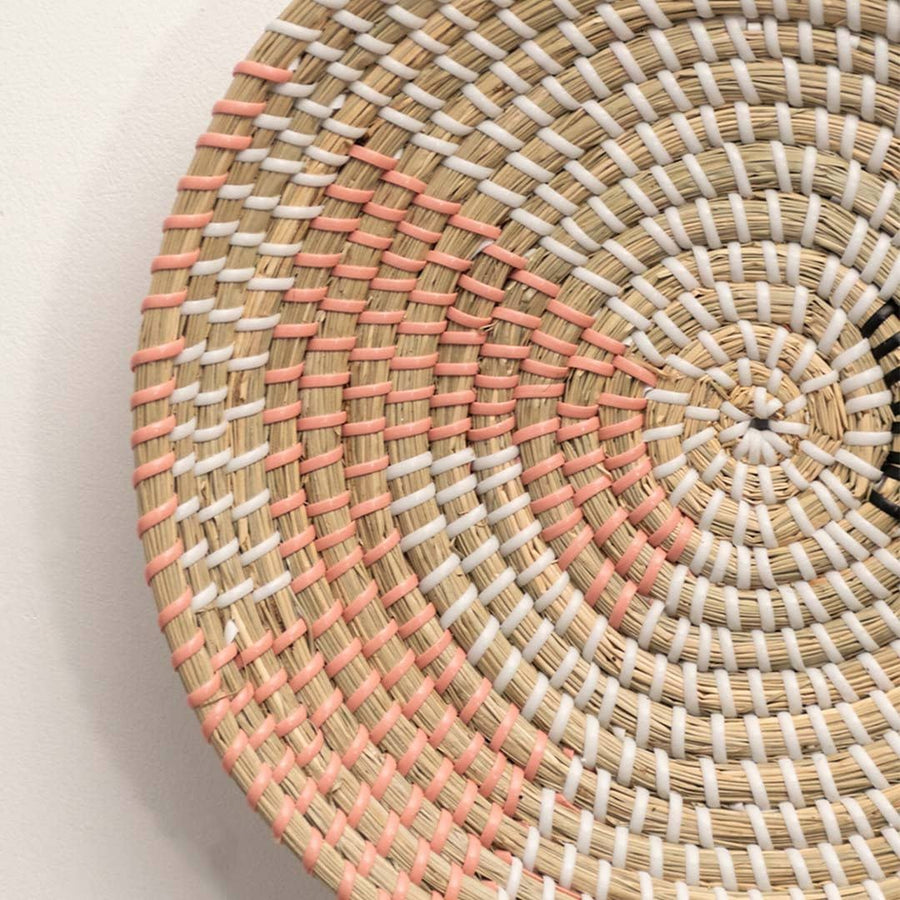 Detailed closeup of handcrafted natural seagrass wall basket with pink woven stitched geometric accents for boho decor.