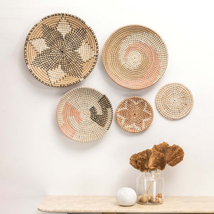 Boho woven wall basket with pink and black swirl pattern hanging on a white wall above a marble table for decor.