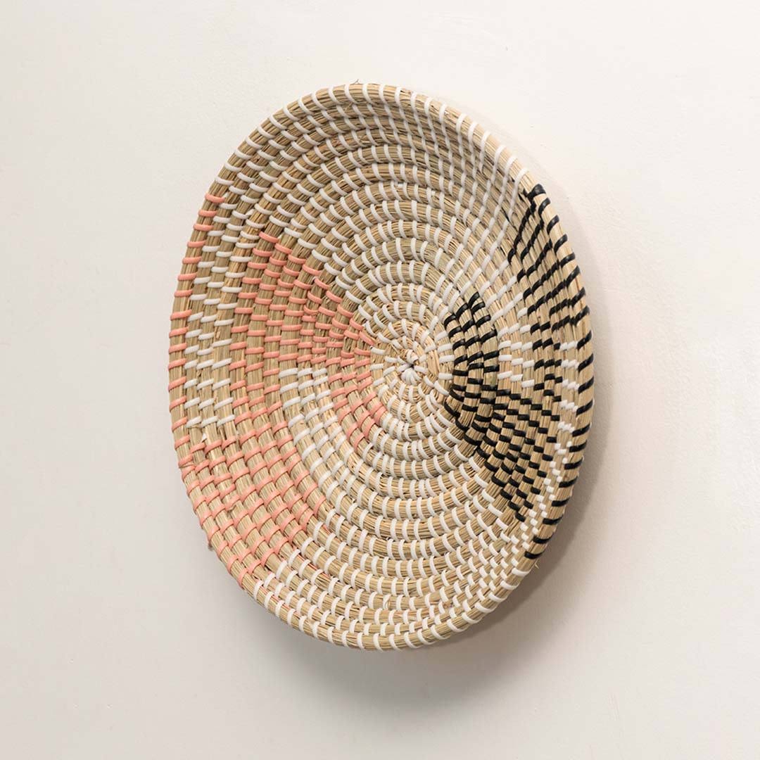 Side view of handcrafted natural seagrass wall basket with pink and black color block pattern for bohemian wall decor.