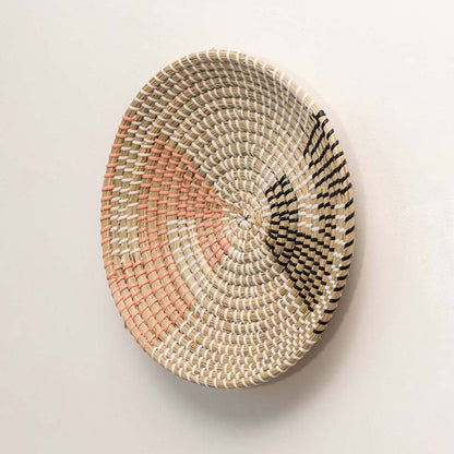 Side view of handcrafted natural seagrass wall basket with pink and black color block pattern for bohemian wall decor.