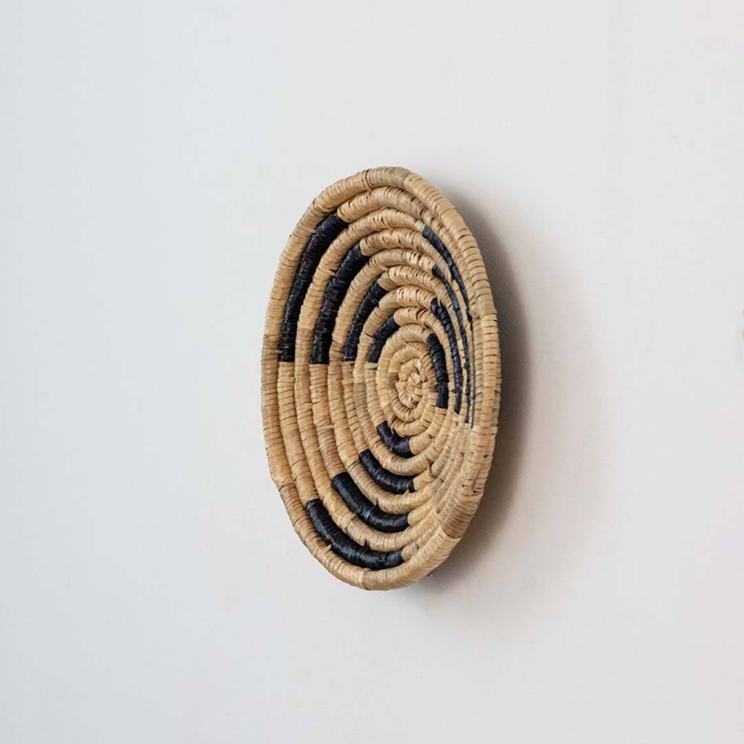 Handwoven seagrass round wall basket decor in natural beige and black with raised spiral woven profile on white background.