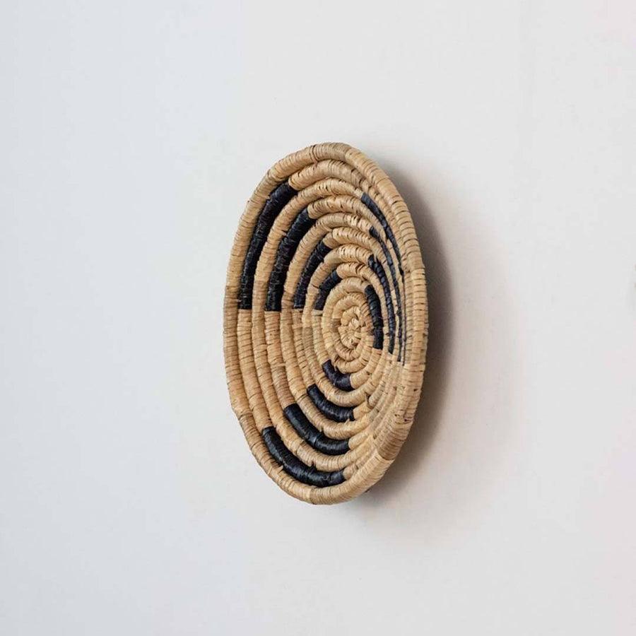 Handwoven seagrass round wall basket decor in natural beige and black with raised spiral woven profile on white background.