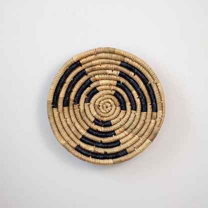 Handwoven seagrass round wall basket decor in natural beige and black with spiral woven pattern displayed on white background.