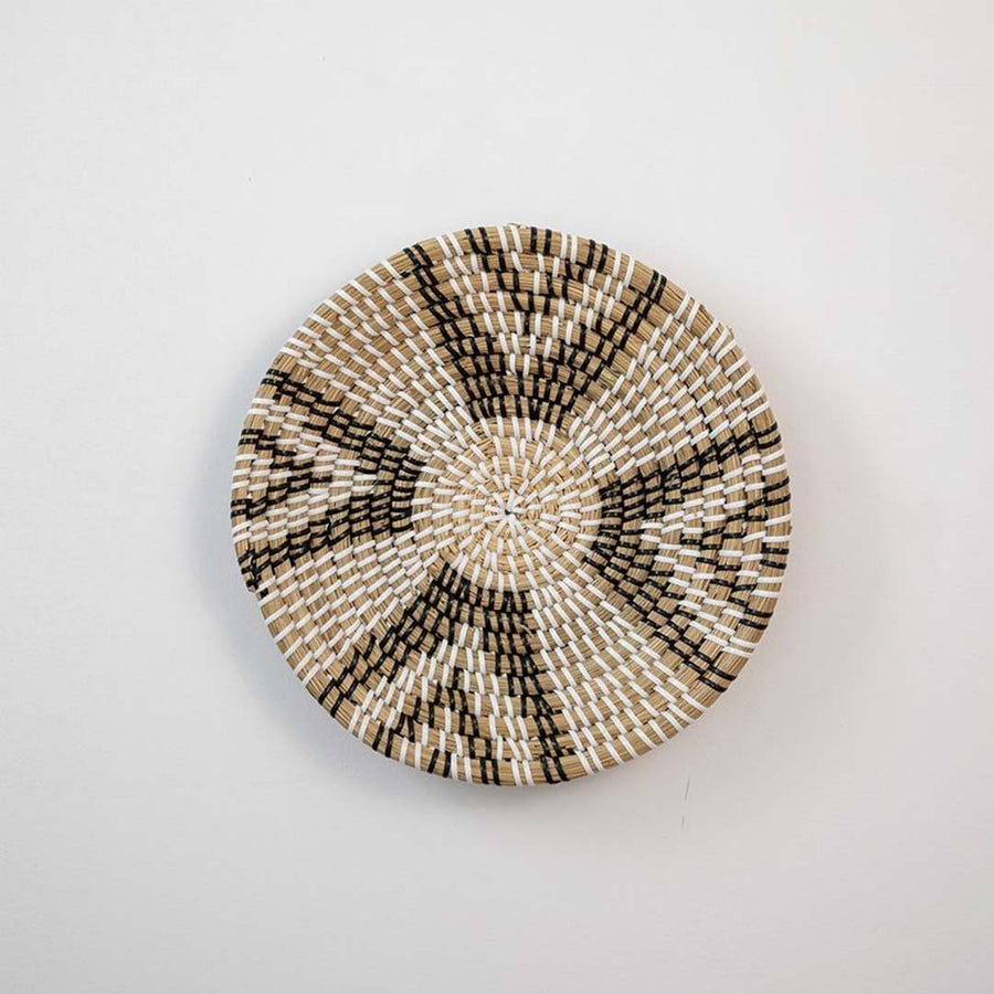 Handwoven seagrass round wall basket decor in natural beige and black with geometric woven pattern displayed on white background.