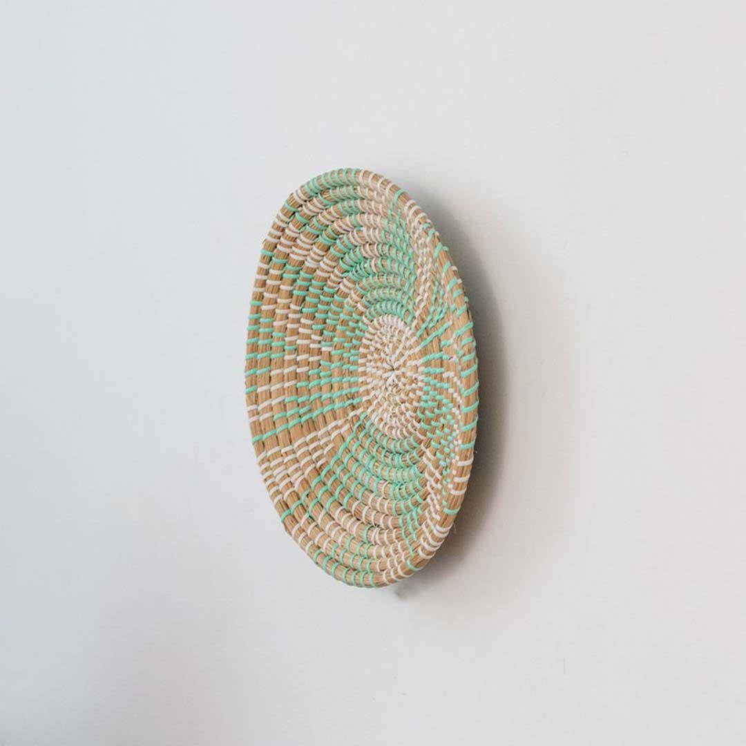 Handwoven seagrass round wall basket decor in natural beige and teal with raised spiral woven profile on white background.