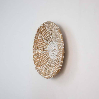 Handwoven seagrass round wall basket decor in natural beige with white spiral woven profile shown on white background.