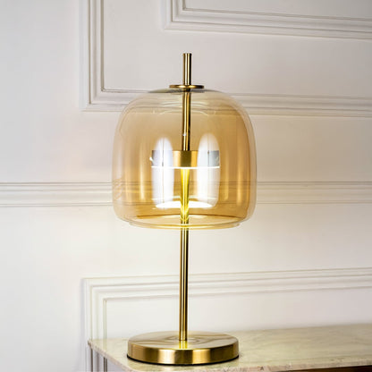 Gold metal table lamp with amber glass shade glowing softly on white background for elegant modern home decor.