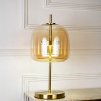 Gold metal table lamp with amber glass shade glowing softly on white background for elegant modern home decor.
