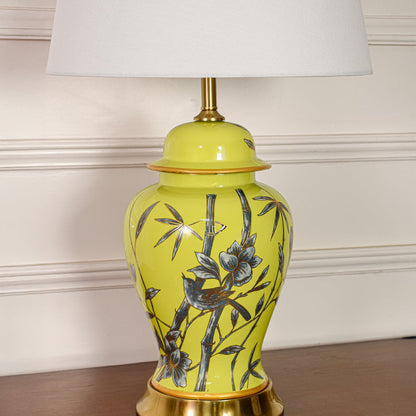 Closeup of yellow ceramic table lamp showing detailed bamboo bird artwork smooth glazed finish and gold metal accents.