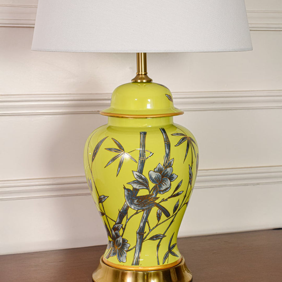 Closeup of yellow ceramic table lamp showing detailed bamboo bird artwork smooth glazed finish and gold metal accents.
