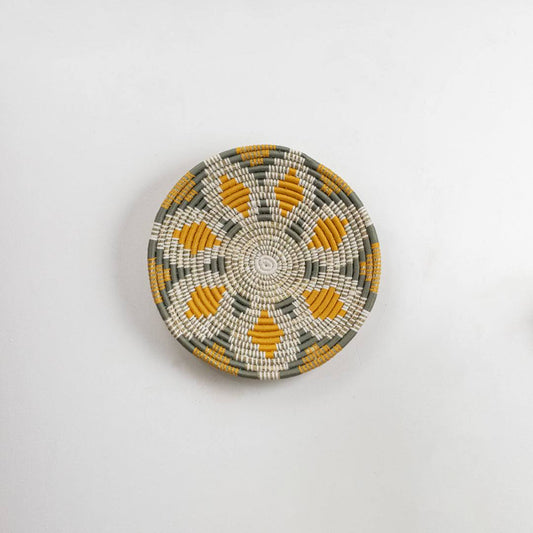 Round handcrafted seagrass wall basket with white and mustard pattern for boho home décor on white background image.