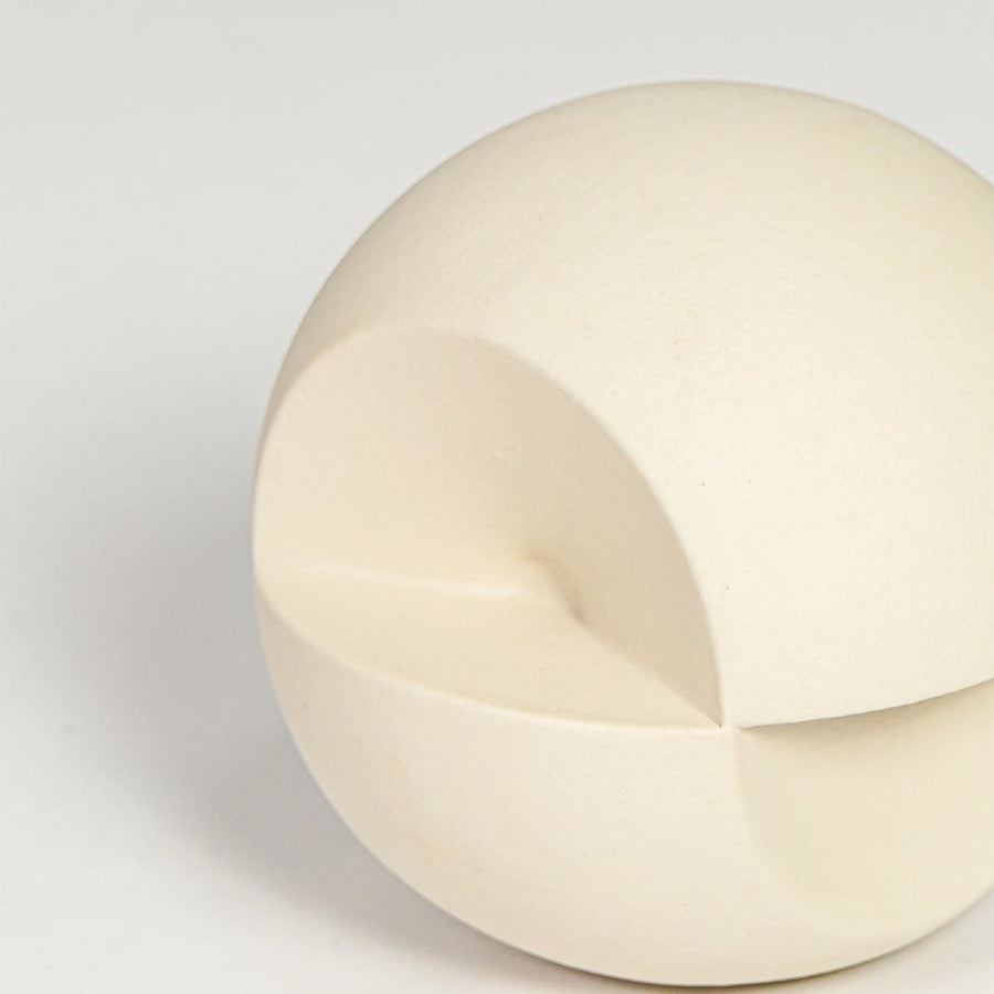 Closeup of cream ceramic spherical decor piece showing carved opening matte texture and minimalist sculptural form.