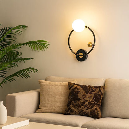 A modern metal wall light with a round glass globe mounted beside a sofa on a beige wall creating warm ambient lighting and enhancing elegant contemporary décor.