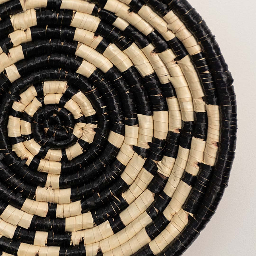 A closeup view of the natural and black rattan wall decor plate showing its textured geometric weaving and handcrafted spiral design for warm earthy decor styling.