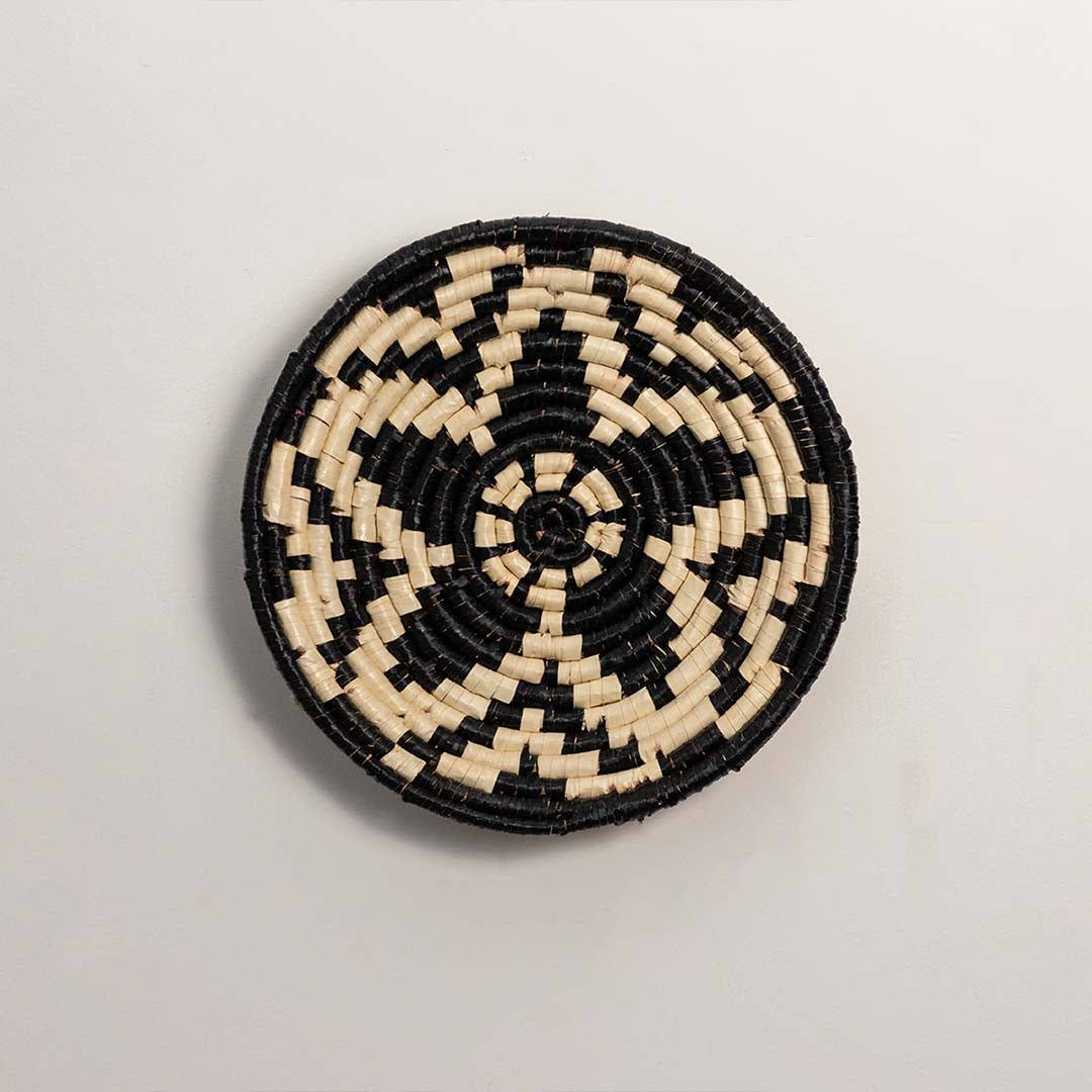 Round handcrafted black and cream seagrass wall basket with woven geometric floral star pattern on white background image.