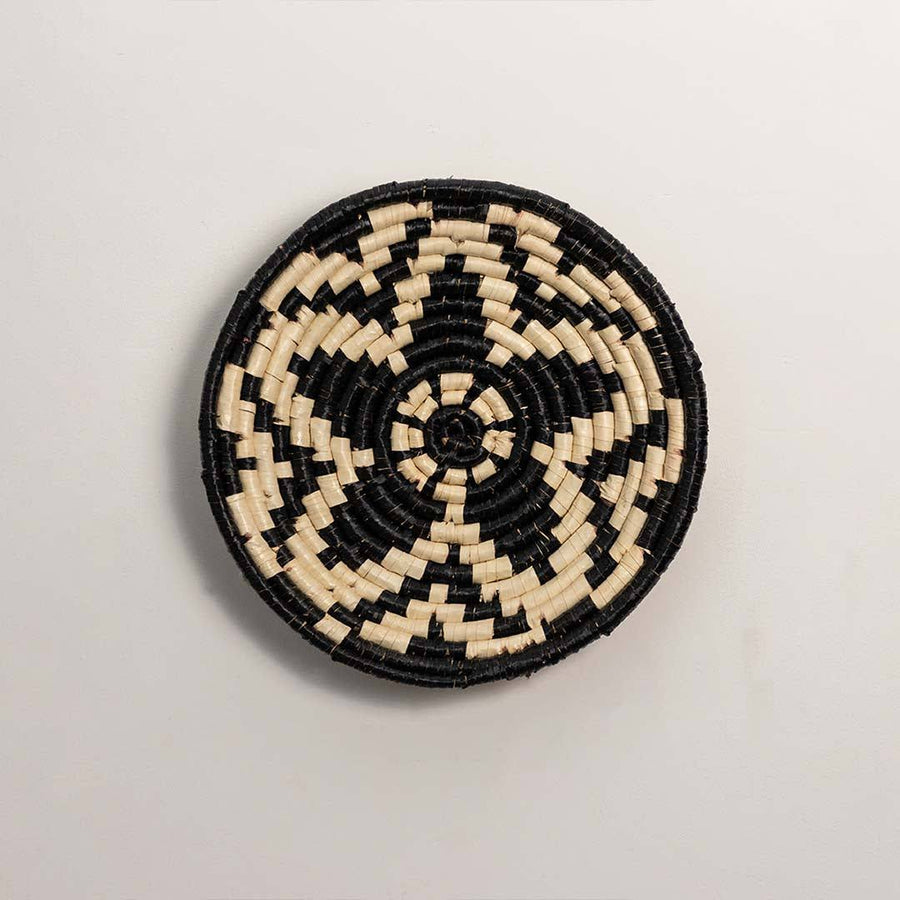 Round handcrafted black and cream seagrass wall basket with woven geometric floral star pattern on white background image.