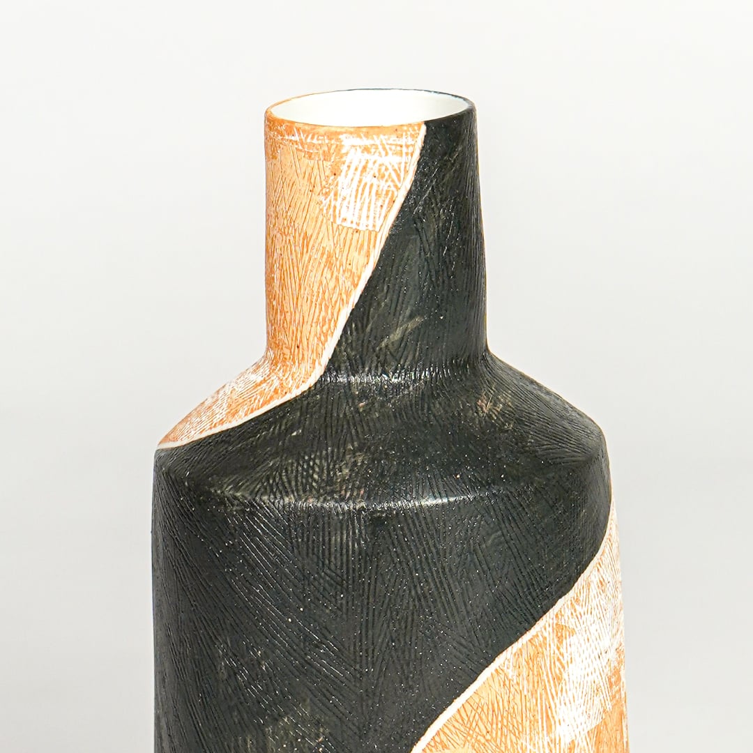 Close view of orange and black ceramic vase highlighting textured finish sculpted neck and modern artistic form.