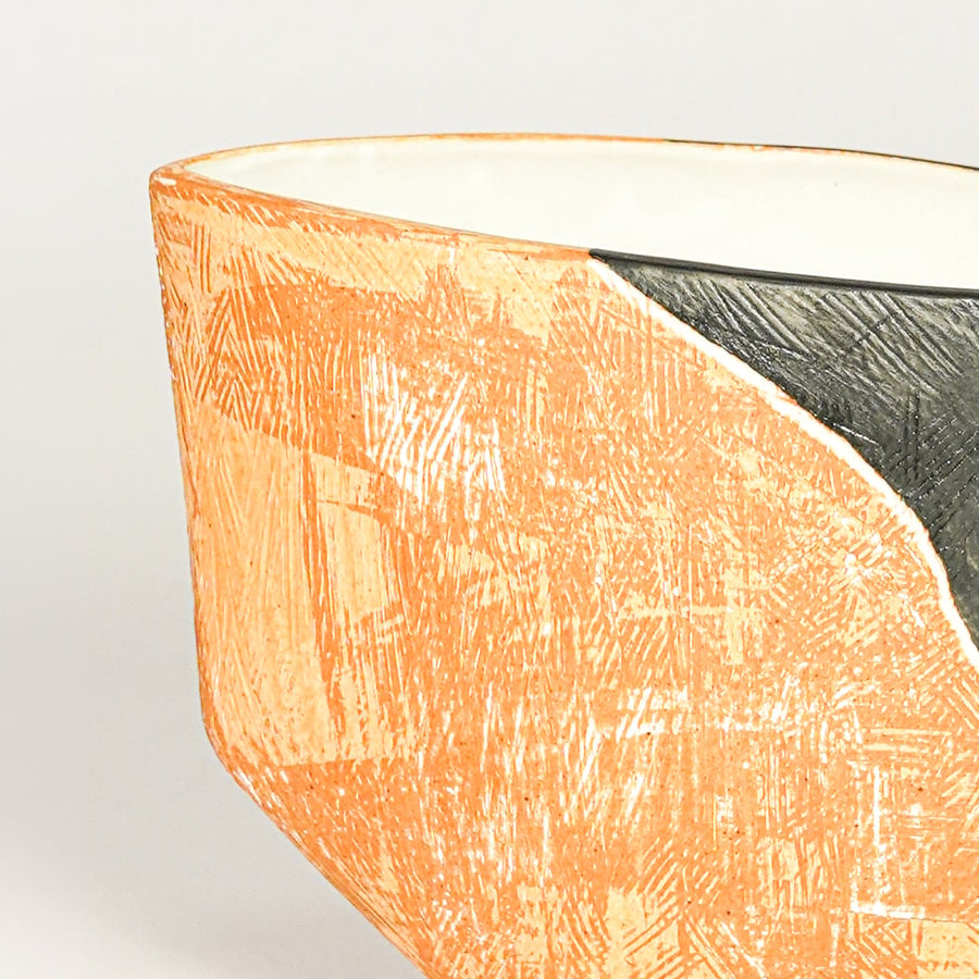 Close view of orange and black ceramic planter highlighting textured surface angled rim and artistic sculptural finish.