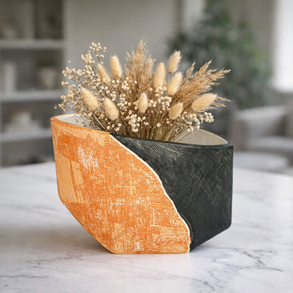 Orange and black textured ceramic decorative planter styled with dried flowers on marble surface in modern home interior.