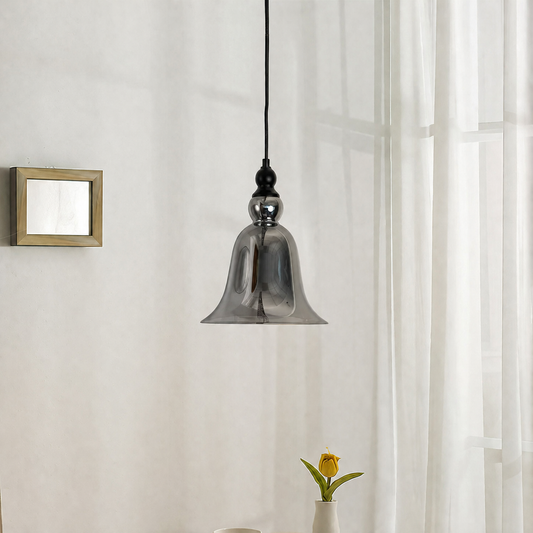 A modern pendant light with a bell-shaped smoked glass shade hanging from a black cord in a bright room with sheer white curtains.