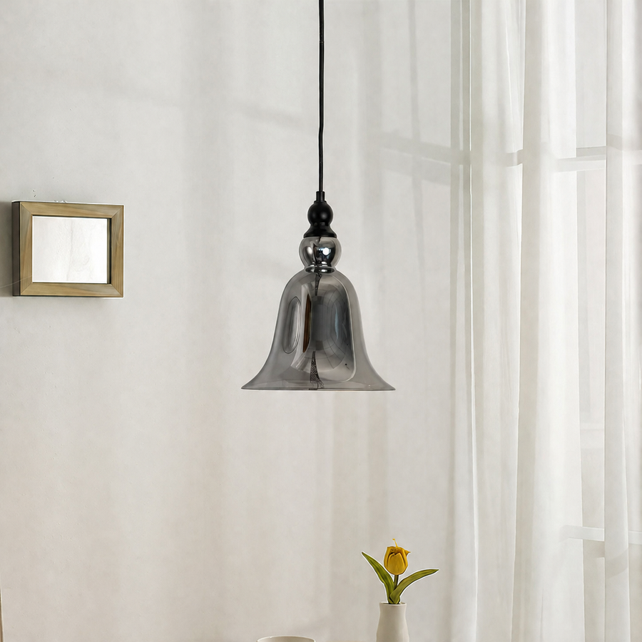 A modern pendant light with a bell-shaped smoked glass shade hanging from a black cord in a bright room with sheer white curtains.