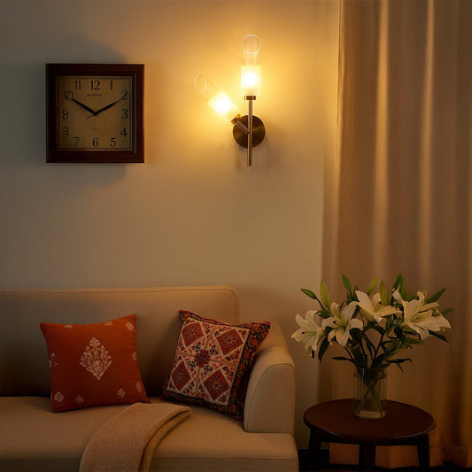Brushed gold dual wall light with frosted glass tubes glowing on white background adding soft warm lighting to modern living bedroom and hallway interiors.