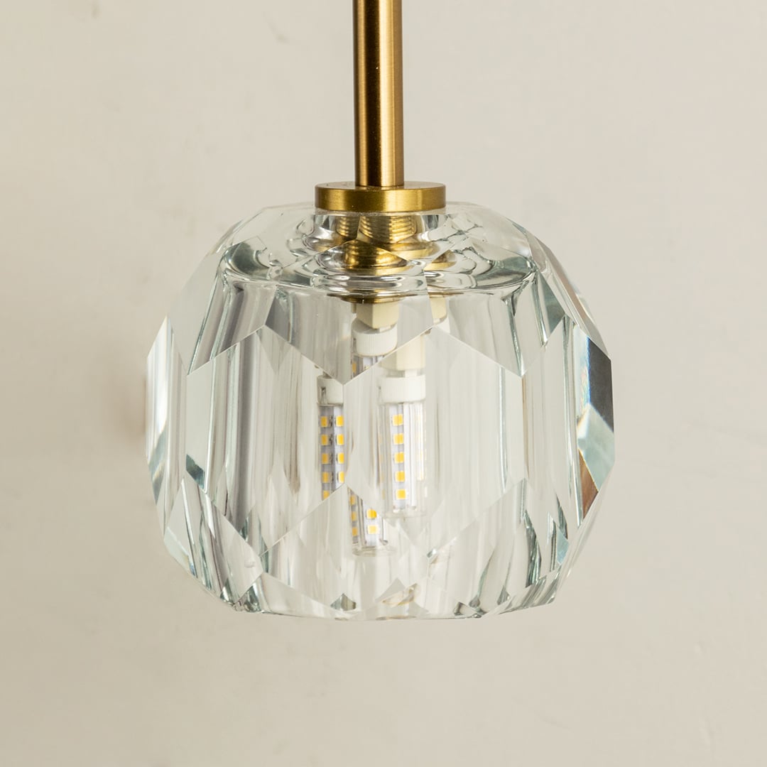 A closeup of the gold metal wall light highlighting the detailed faceted crystal shade and smooth metallic arm for a luxurious modern lighting finish.