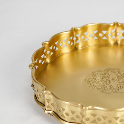 Closeup view of antique gold metal serving tray highlighting ornate engraving and decorative scalloped edges.