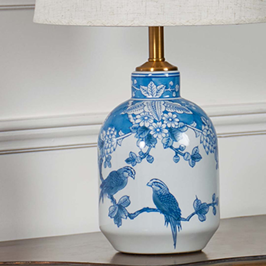 Detailed closeup of the blue and white ceramic lamp base featuring intricate bird and floral artwork with metallic gold hardware.