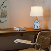 Blue and white floral ceramic table lamp with fabric shade placed on a wooden desk creating warm ambient lighting indoors.
