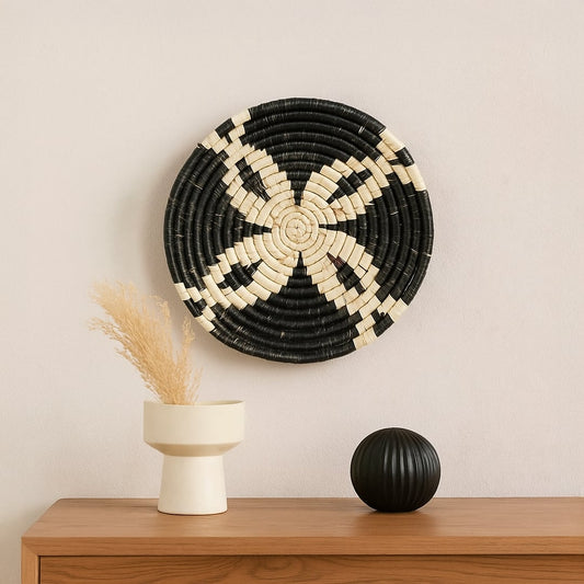 Handwoven round wall basket Decor with bold black and natural fiber pattern styled on a neutral wall above a wooden console with minimal vases creating a modern earthy interior look.