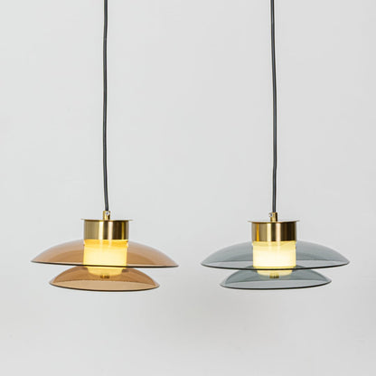 Grouped amber and smoky grey pendant lights with gold metal tops shown with lights on creating warm soft illumination for contemporary spaces.