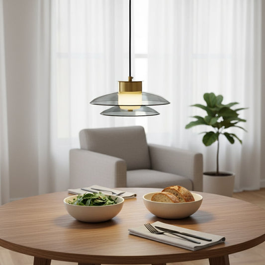 Modern grey glass pendant light with gold metal fitting glowing warmly above a round dining table creating a soft cozy atmosphere in a minimal living space.