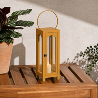 Playful mustard yellow wooden frame lantern candle holder with a circular loop metal handle sitting on a slatted wooden patio table.