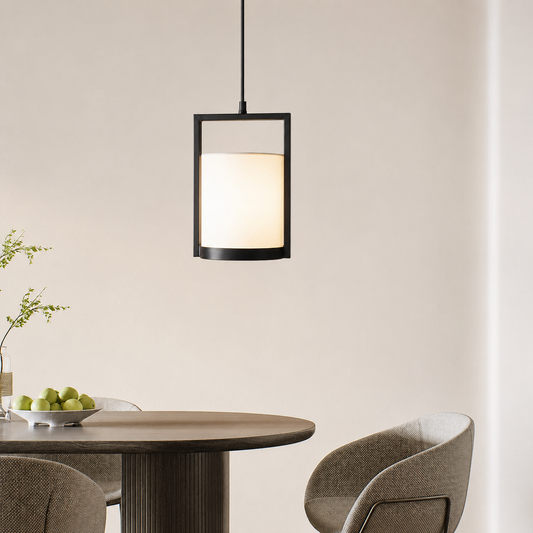A modern rectangular pendant light with a black metal frame and a glowing warm white fabric shade, hanging above a dining table with chairs and a bowl of green apples in a minimalist room.