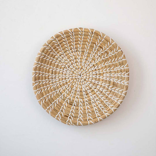 Round natural handwoven seagrass wall basket with neutral sunburst pattern on simple white background for boho accent.